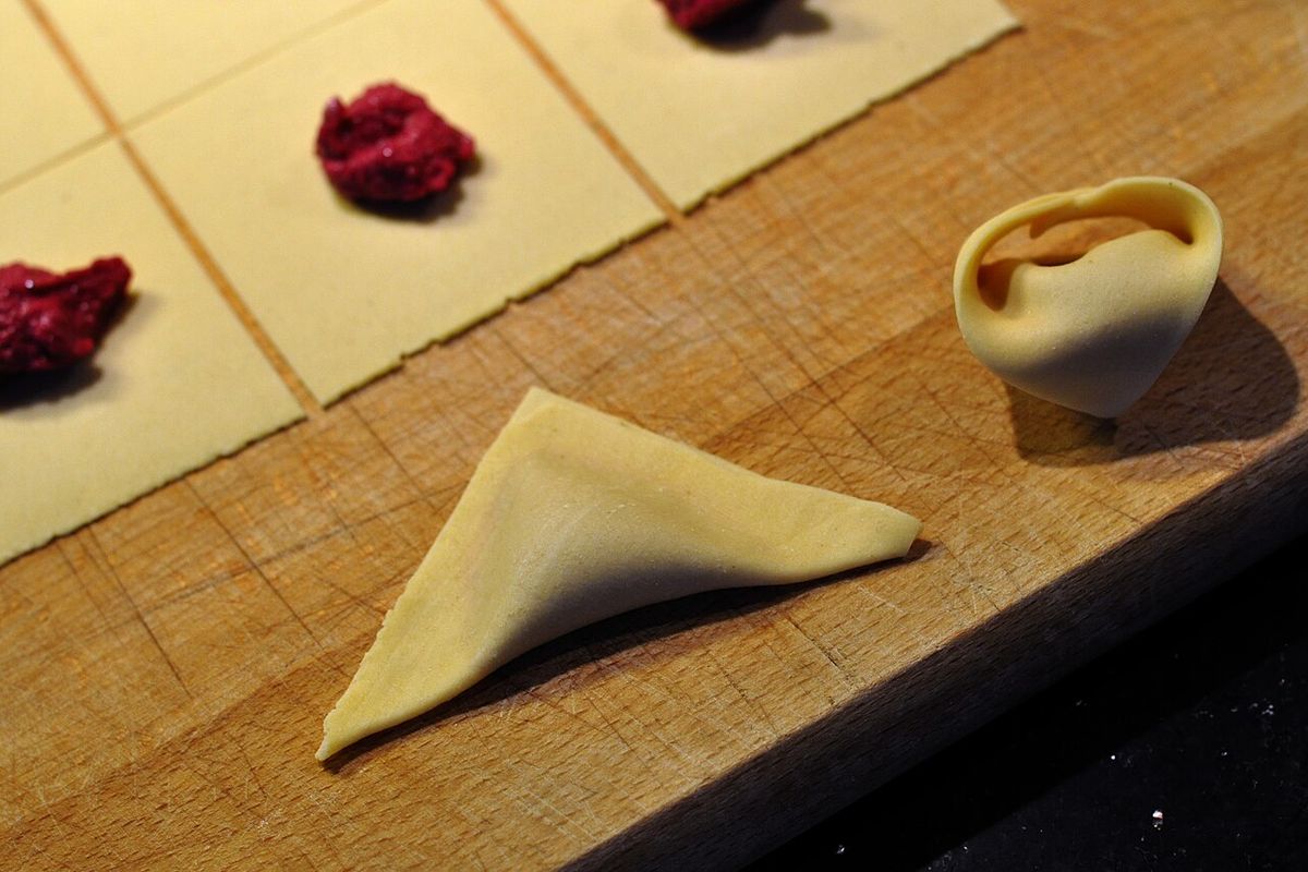 Tortellini sendo fechados à mão sobre tábua de madeira