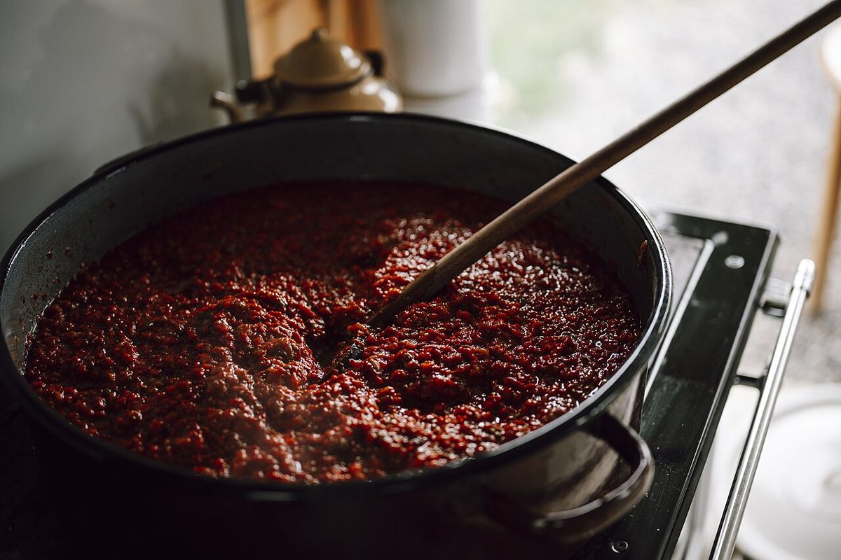 Panela grande de molho de tomate cozinhando com colher de pau